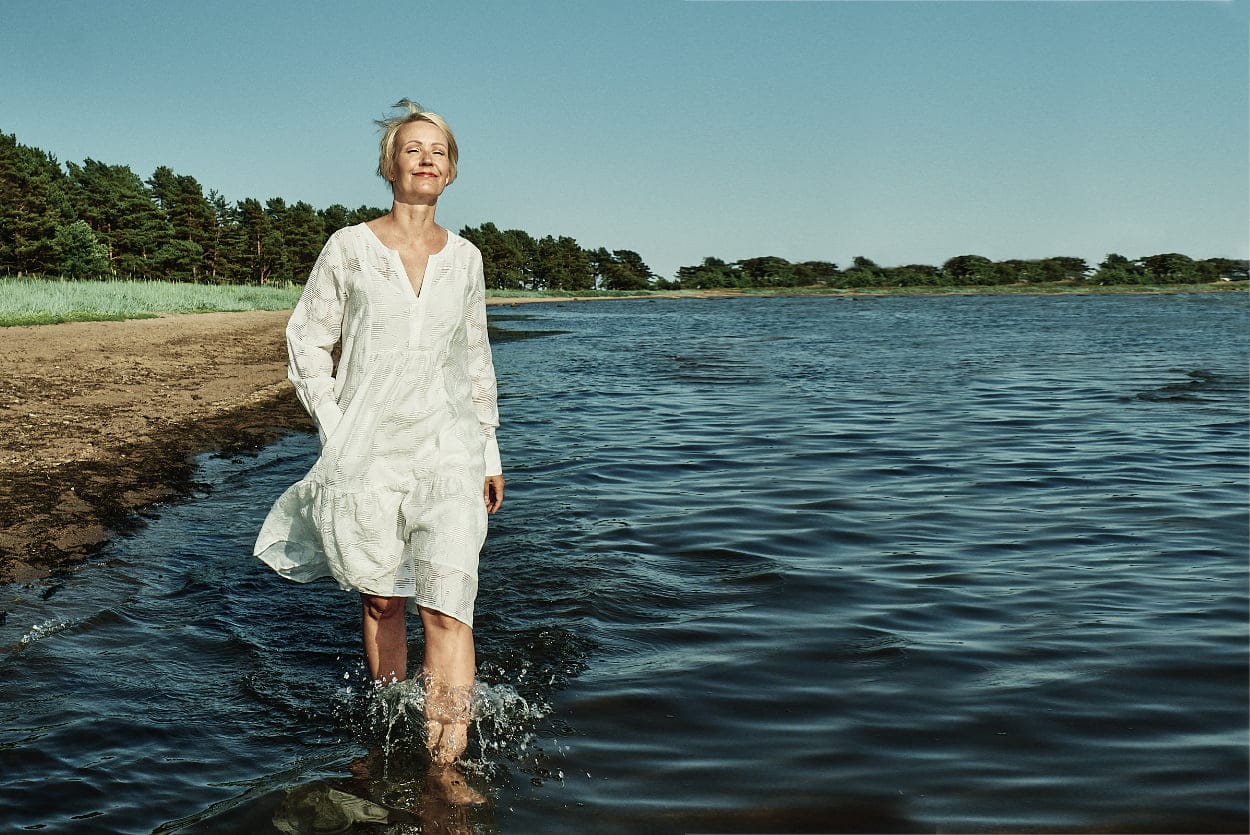 Malou C summer campaign: woman in a white linen dress wading into the sea