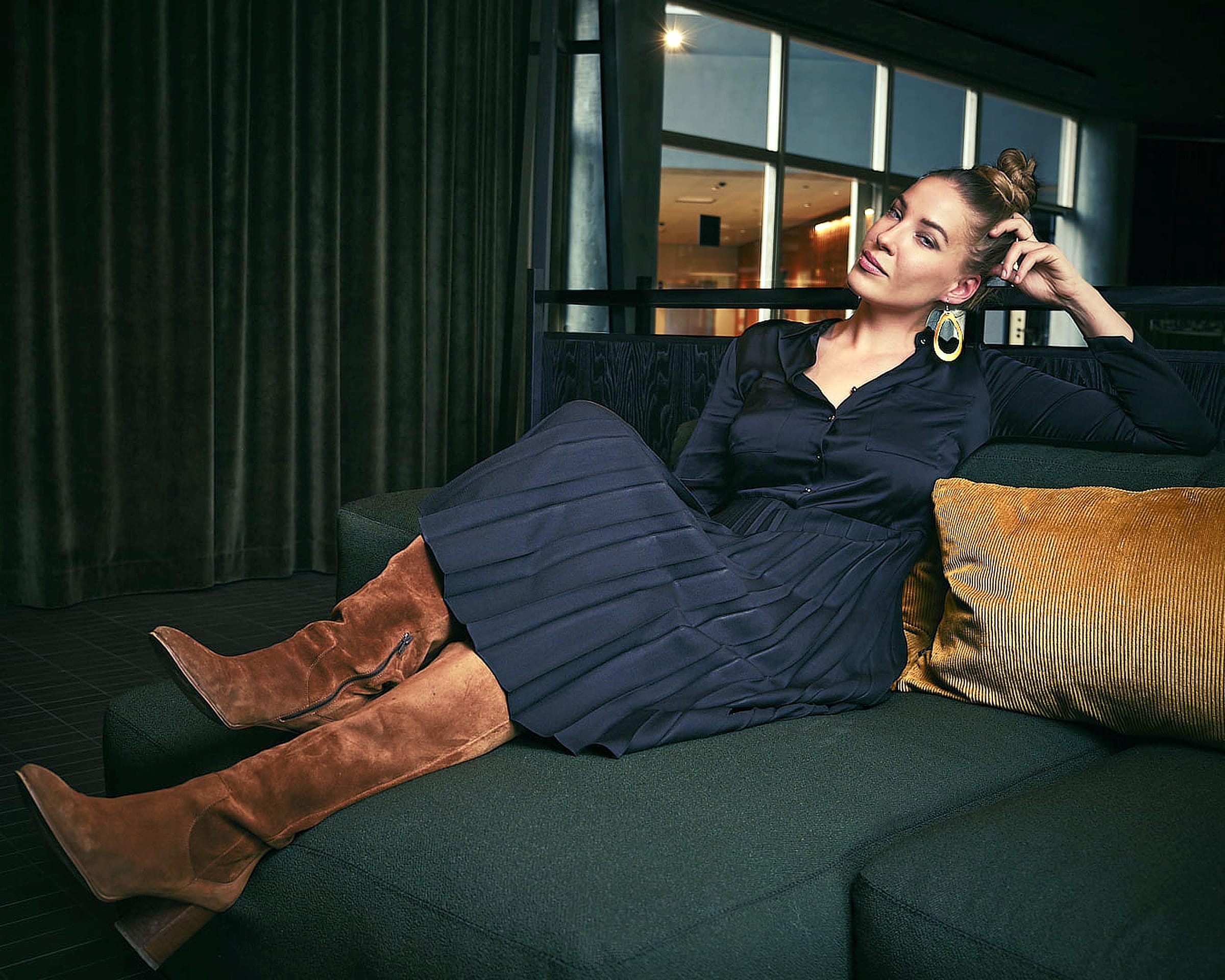 Malou C campaign: model in a navy pleated dress and suede boots in a hotel lounge